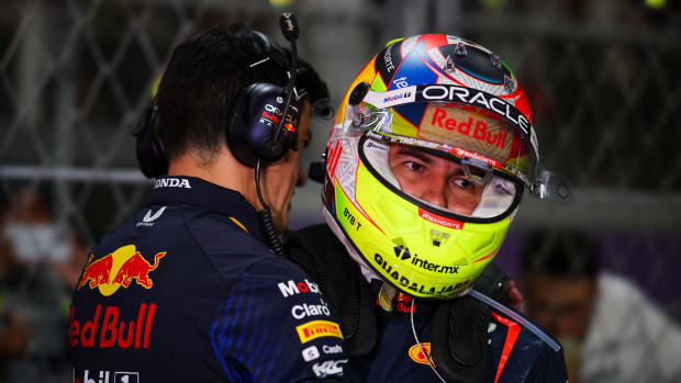 Hombre le dice algo al oído a Checo Pérez mientra trae su casco de piloto.